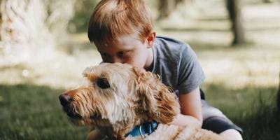 A young boy is petting his dog outside and on green grass.